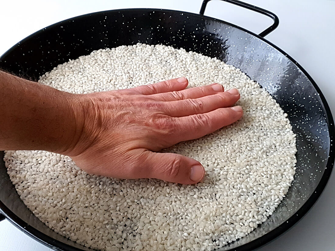 Hand flattening rice grains in a paella pan.
