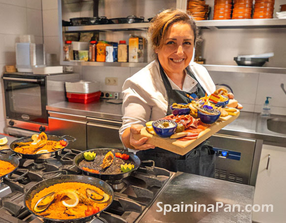 Woman behind cooking stove holding a mixed tapas dish in a professional kitchen