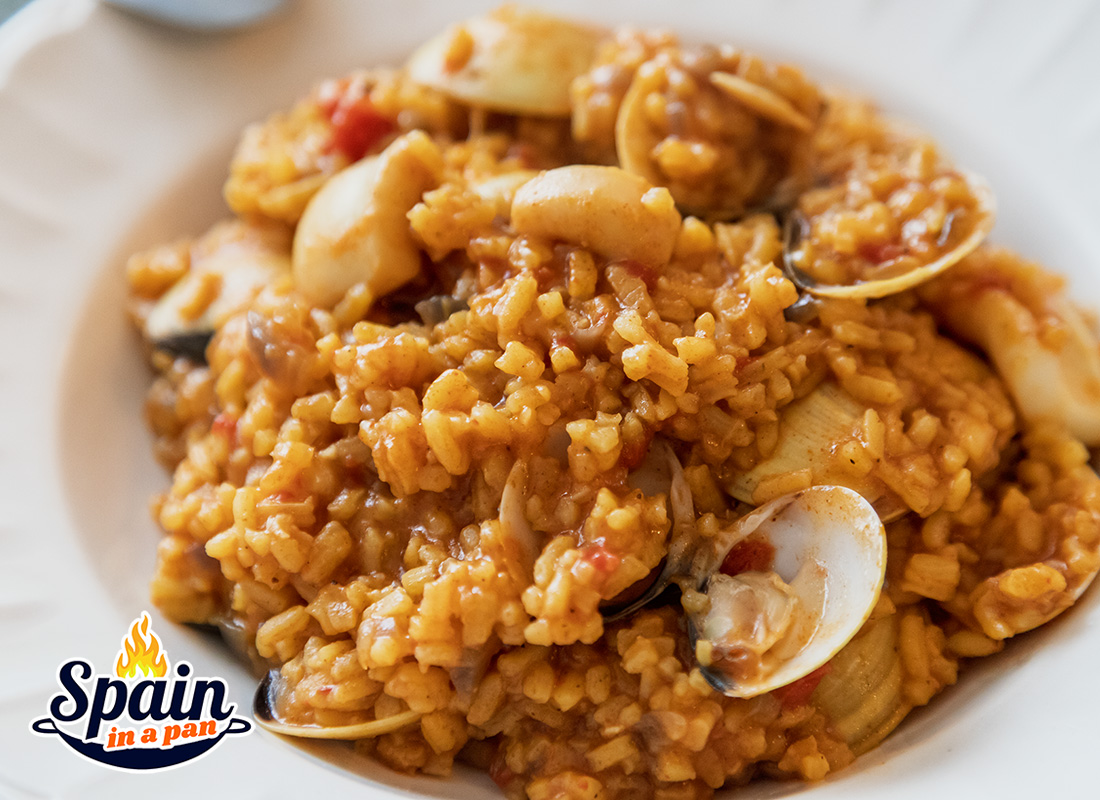 Spanish, creamy rice with venus clams on a white plate.