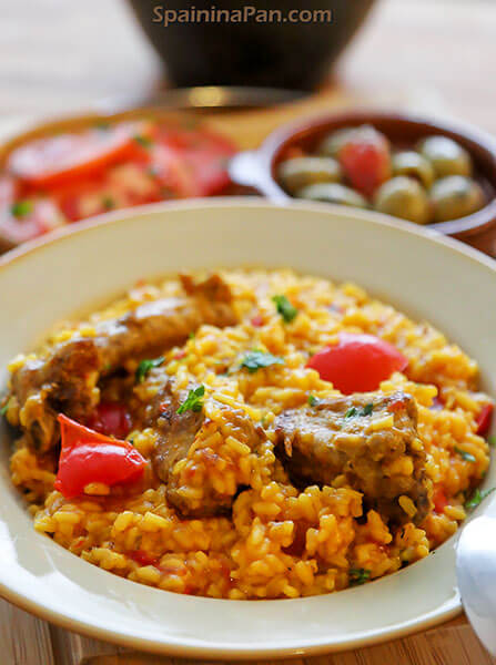 Spanish rice and pork ribs stew on a plate with olives in the background.