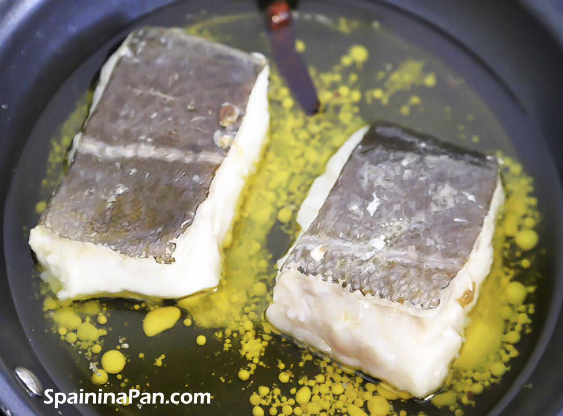 Two cod slices in a pan releasing gelatin for the pil pil sauce.