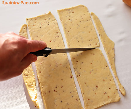 Cutting pestiños dough rectangles on a white table.