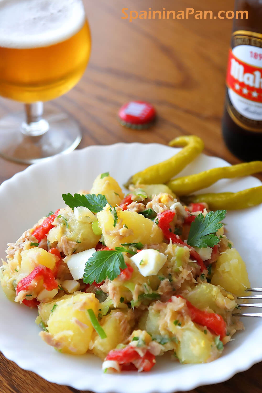 Spanish mixed potato salad on a plate with a bottle and glass of beer.