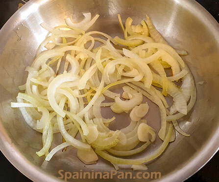 Onion cut julienne style in a stainless steel bowl.