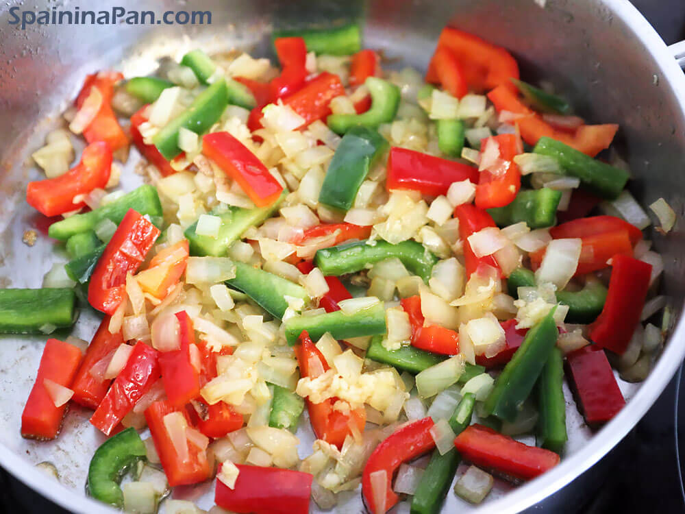 Preparing a sauté for the chicken and chorizo paella in a frying pan.