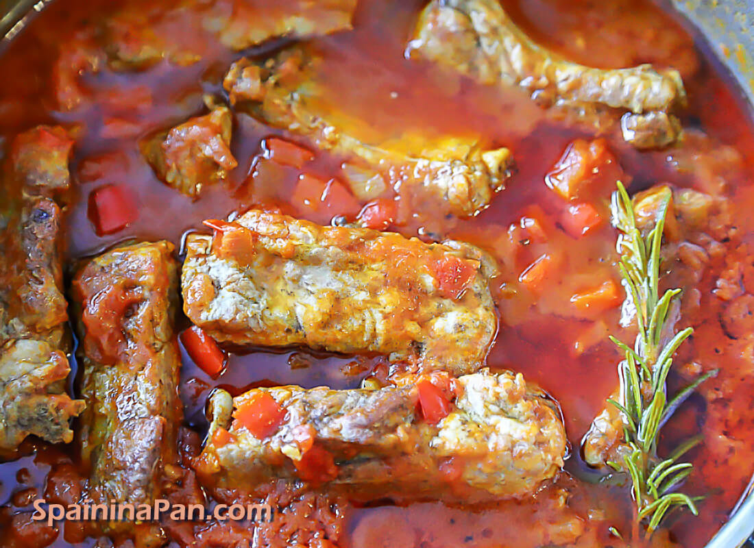Pork ribs simmering in tomato sauce in a pan. Pork ribs simmering in tomato sauce in a pan.