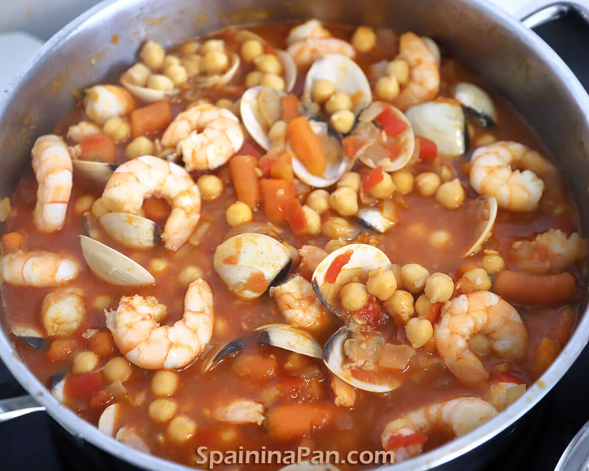 Spanish chickpea and seafood stew in a metal pot.
