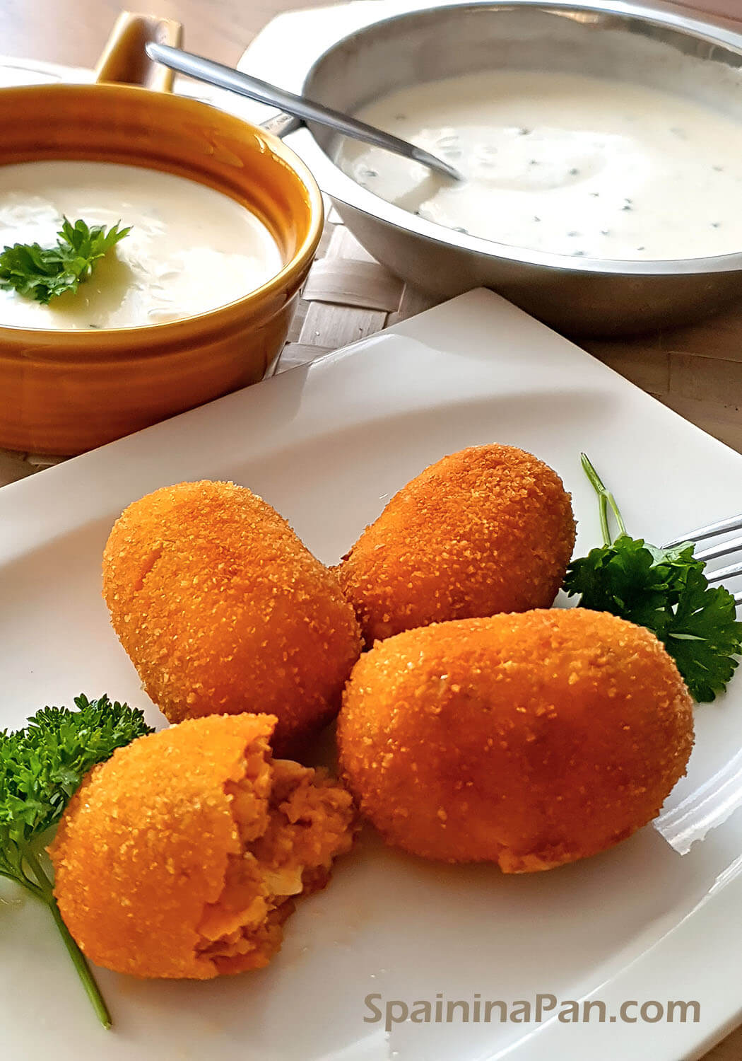 Spanish chistorra and eggs croquettes on a plate with dip sauce in the background.