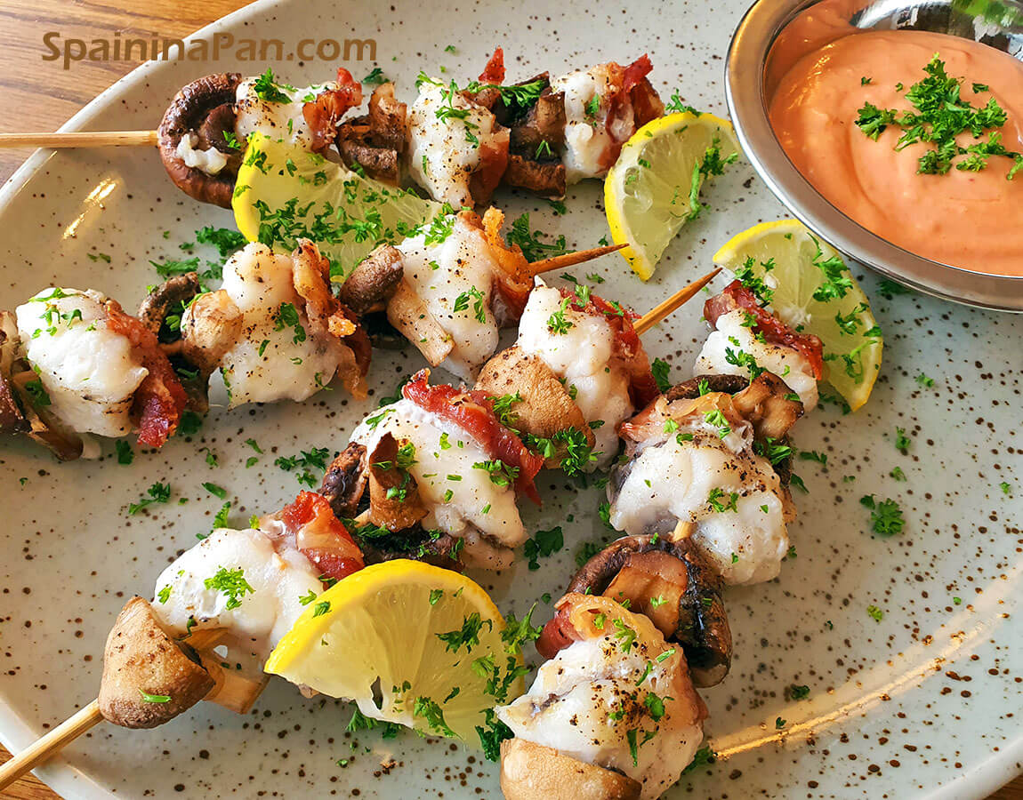 Spanish monkfish with mushroom brochette on a plate with red sauce. Spanish monkfish with mushroom brochette on a plate with red sauce.