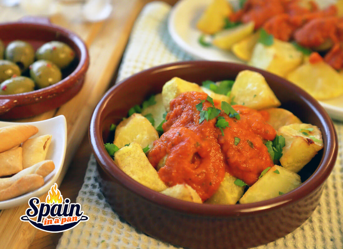 Patatas bravas with tomato salsa brava in a clay tray.