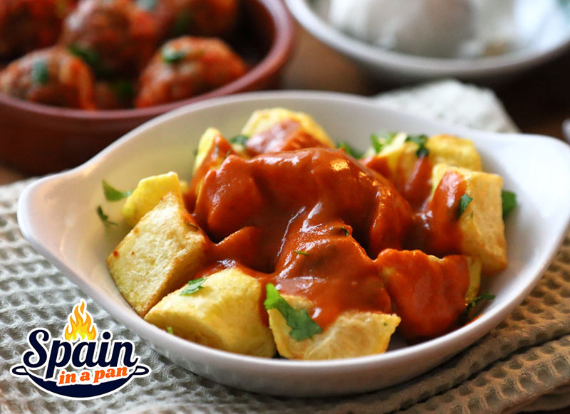 Patatas bravas with paprika based salsa brava in a white tray.