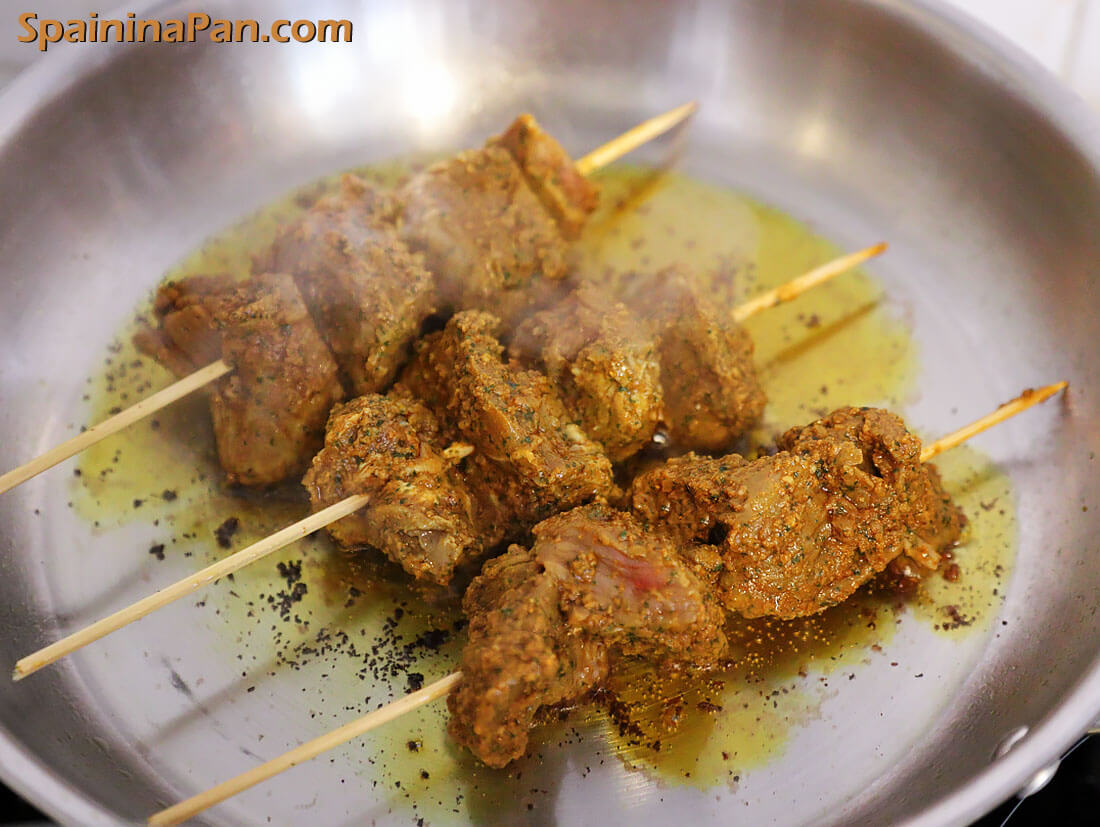 Pinchos morunos frying in a regular steel pan.
