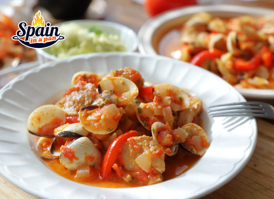 Spanish pork loin with clams stew on a plate with side dishes.